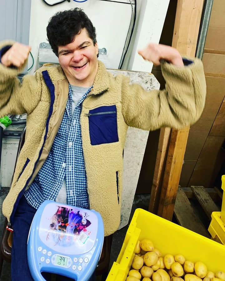 A man in a fleece jacket beaming and flexing his arms at the produce warehouse where he works.